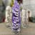Clear glass stemless champagne flute, with purple tissue paper on the inside. The glass reads "Bride" in white cursive font and a heart acting as the dot for the "i"