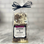 Clear cello food packaging showing contents of white chocolate bark with bits of dark cookie with square front label and tied with a bow