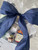 Close up of bow on wrapped gift basket; a large navy blue bow, with an accent ribbon that is white with sparkly silver trees Close up of bow on wrapped gift basket; a large navy blue bow, with an accent ribbon that is white with sparkly silver trees