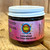 Clear glass jar with white lid showing contents of dark red onion marmalade with a pink and purple front label