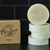 Stack of four white round shave soap bars and a light brown square box with black lettering 