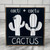 Square wood block with black background with white lettering and a white cactus with a star and another white cactus with a bowtie.