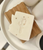 off white bar of soap in the shape of Arizona with a cut out in the shape of a saguaro cactus displayed on a wood soap saver dish