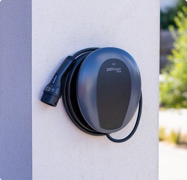 Pod Point home charger mounted on a white exterior wall, with cable neatly wrapped.