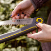 Two hands opening the Compact Duralight Folding Saw using the yellow blade lock