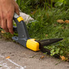 A hand trimming grass at a path edge with the Heavy Duty Rotating Grass Shears, blades turned sideways