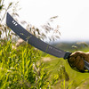 A gloved hand swinging the Heavy Duty Machete through tall grass