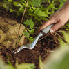 A hand using the Heavy Duty Weeder to lever a weed out of soil beside a rock