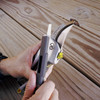 Two hands using the carbide sharpener on the multitool to restore the edge of a Pro Series forged steel pruner blade on a wooden deck