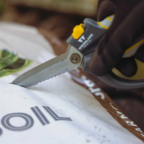 A gloved hand cutting open a soil bag with the Super Duty Utility Snips
