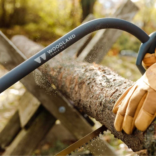 A gloved hand cutting through a log with the Heavy Duty Bow Saw, sawdust flying