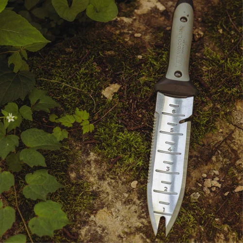 The Hori Hori Garden Knife lying on mossy ground, showing the depth markings and serrated edge