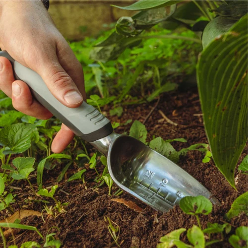A hand digging a planting hole with the Heavy Duty Transplanter in a shade bed