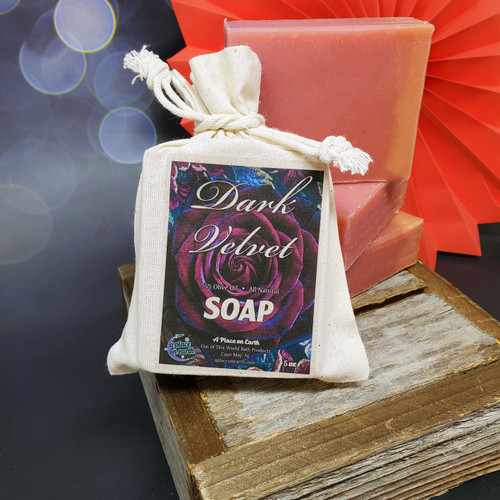 A bar of Dark Velvet soap in its decorative pouch, leaning against a stack of unwrapped bars. 