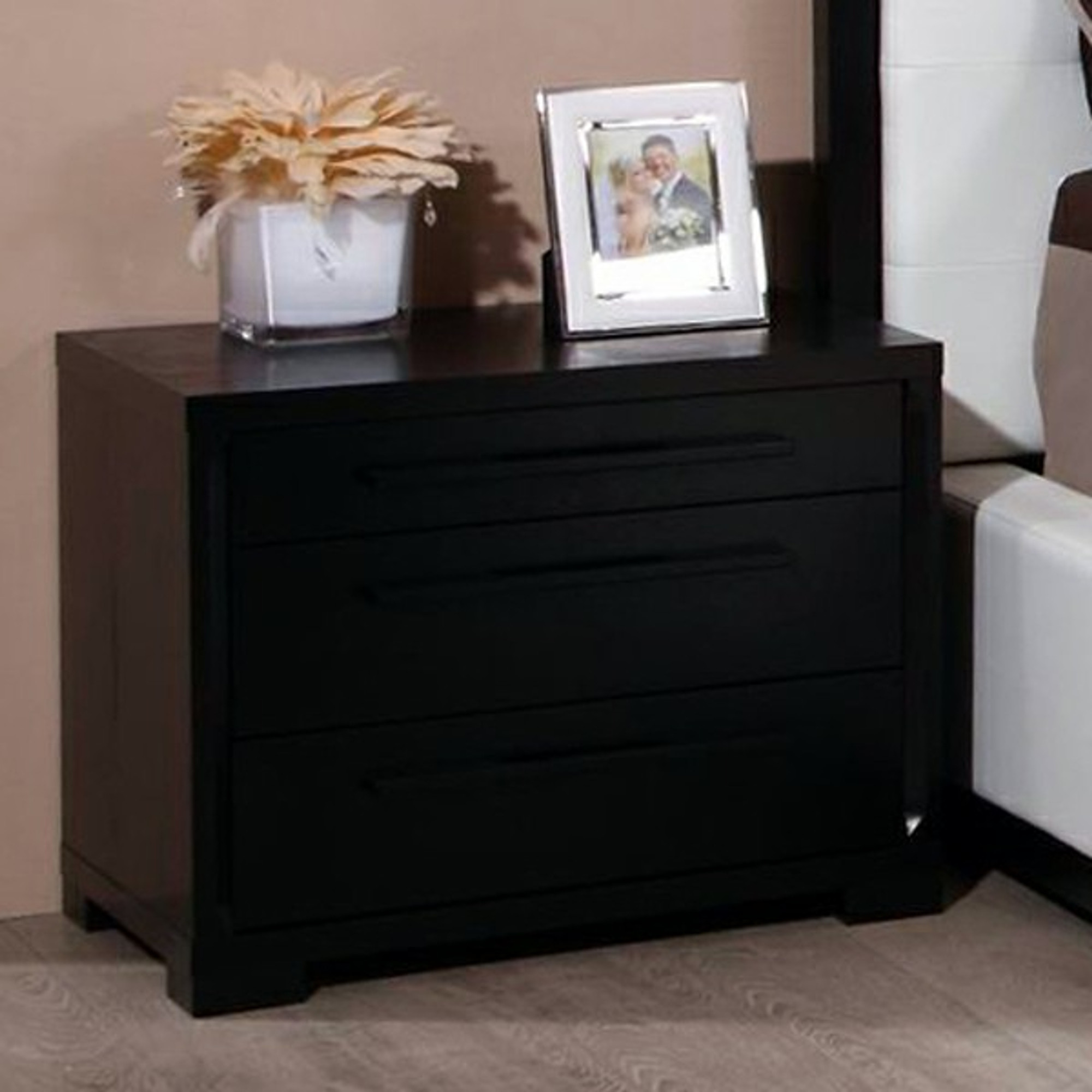 dark wood nightstand with three drawers, the top drawer is the smallest while the bottom drawer is the largest.