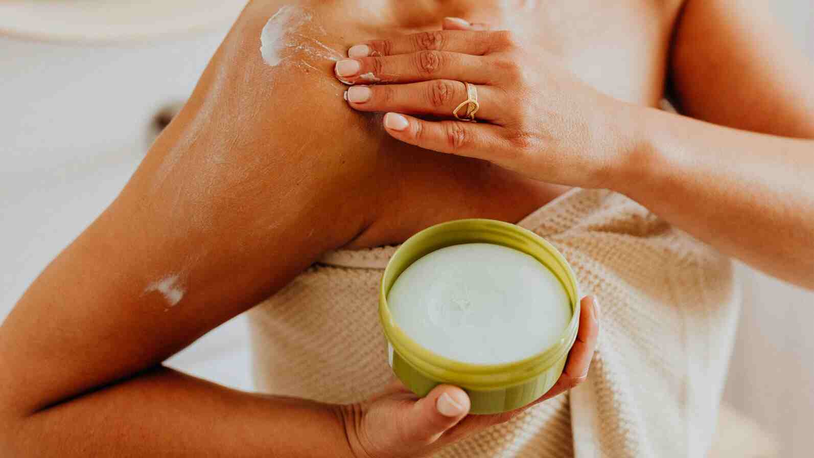 Woman putting cream on body skin.