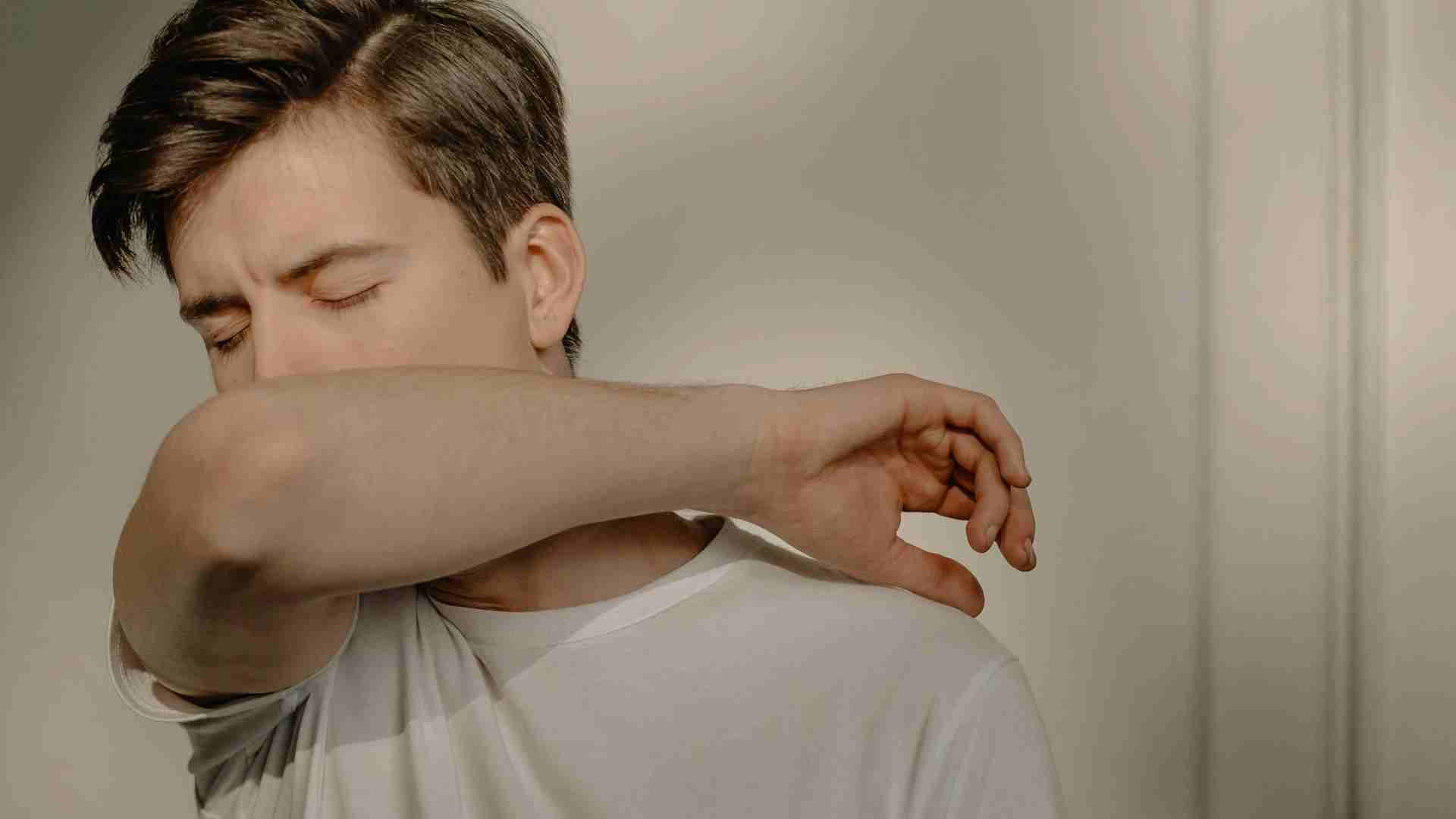 A man with his eyes closed and mouth to his inner elbow, suffering from a dry cough.