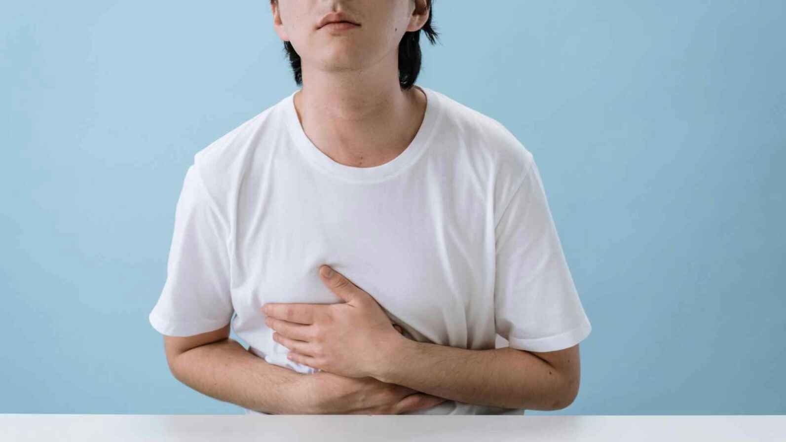A man with his hands on his stomach, displaying signs of discomfort and nausea. 