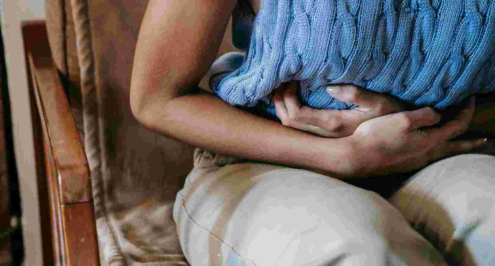 A woman in a chair, hands on her stomach, showing signs of discomfort due to period pain.