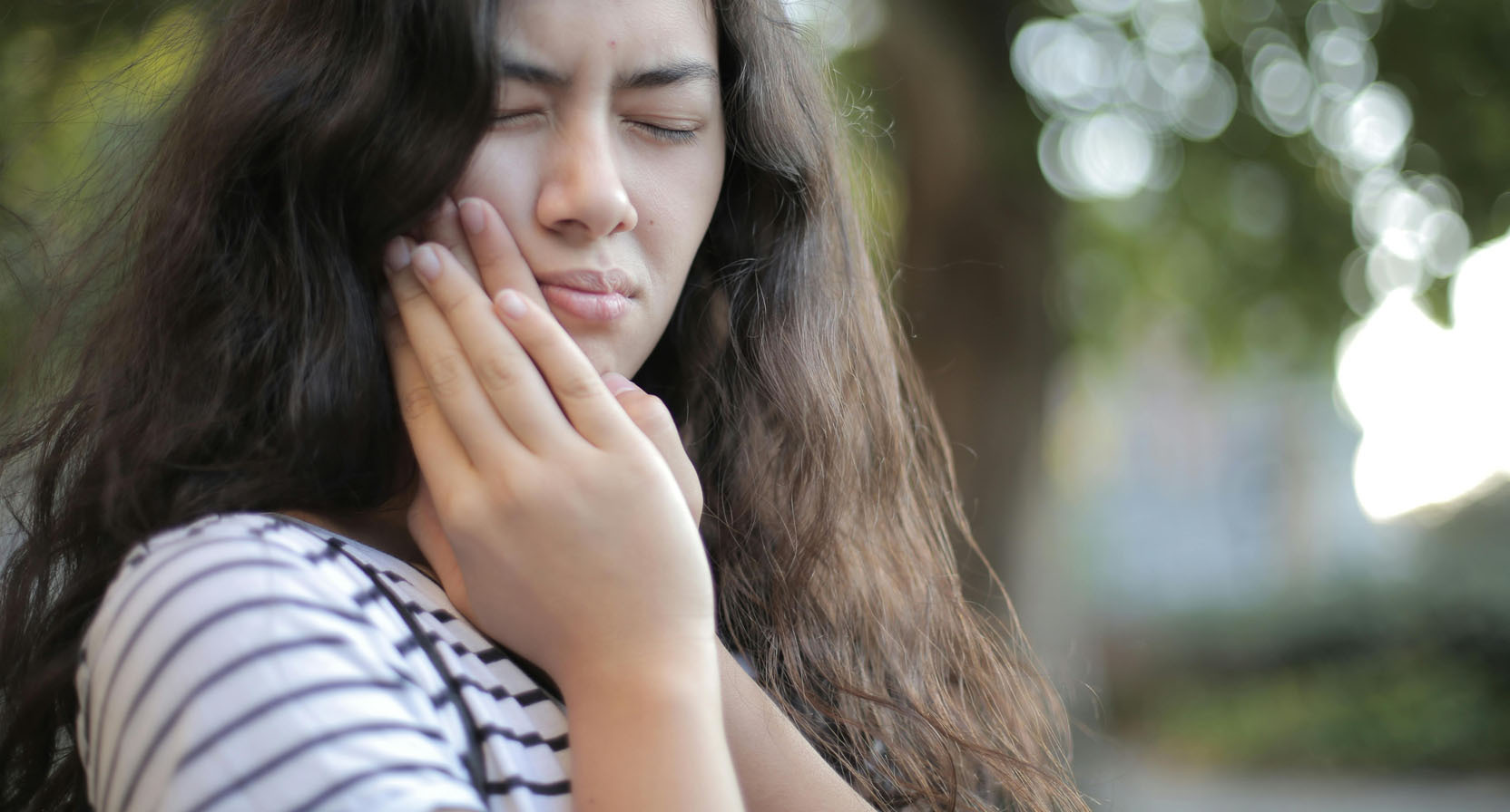 A woman with her hands on her face, expressing discomfort due to a toothache.