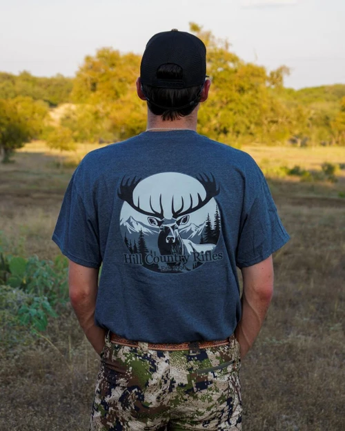HCR T-Shirt - Navy, back view of a person wearing a navy blue T-shirt with a graphic print of a deer, mountain, and forest with the text 'Hill Country Rifles, Est. 1996' on the back.
