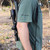HCR T-Shirt in Moss Green, close-up of the sleeve with 'Hill Country Rifles' logo, outdoor wooded background.