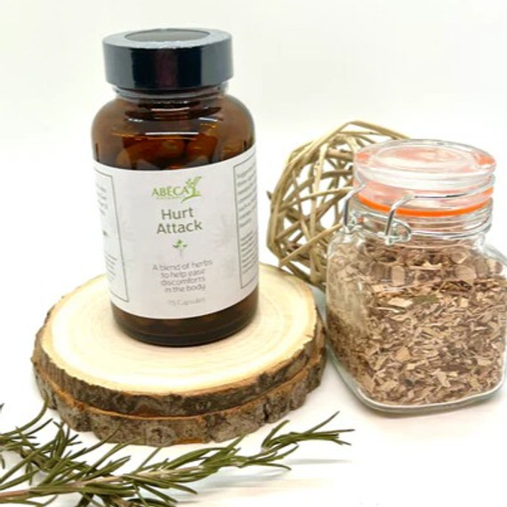 Abeca Naturals Hurt Attack Capsules 100-count bottle, a herbal supplement for headaches, cramps, and minor aches, displayed on a wooden slice with rosemary sprigs and a jar of dried herbs. Abeca Naturals Hurt Attack Capsules 100-count bottle, a herbal supplement for headaches, cramps, and minor aches, displayed on a wooden slice with rosemary sprigs and a jar of dried herbs.
