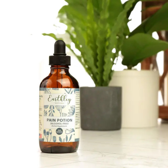 Single 4 oz bottle of Earthley Pain Potion alcohol-free herbal tincture on countertop with green plants in background Single 4 oz bottle of Earthley Pain Potion alcohol-free herbal tincture on countertop with green plants in background