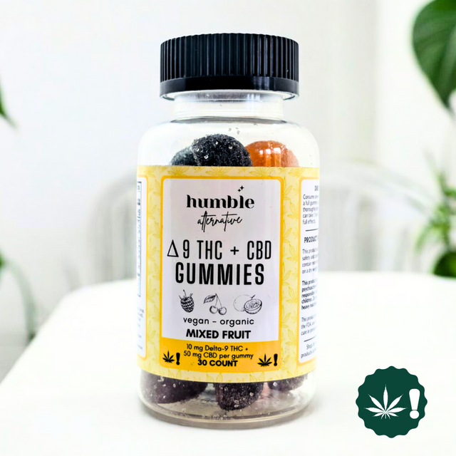 Bottle of Humble Alternative Delta-9 THC + CBD Gummies in Mixed Fruit flavor, vegan and organic, containing 10mg Delta-9 THC and 50mg CBD per gummy, 30-count jar, displayed on a white table with green plant in background.