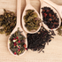 “Assorted loose leaf teas displayed in wooden spoons on a wooden surface, including green, black, and herbal blends for bulk apothecary use.”
