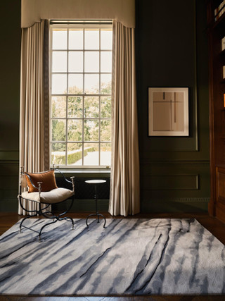 David Rockwell Fjord Flint rug in a dark green panelled room by a tall sash window, with an iron curule chair and side table