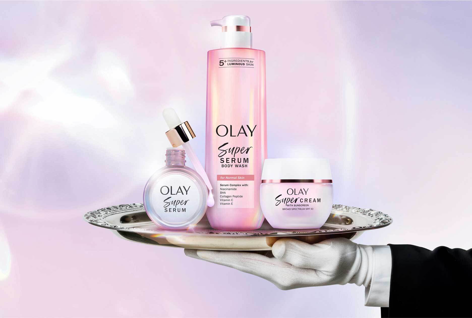 Olay Super Serum skincare set including facial serum, body wash, and face cream for luminous skin, displayed on a silver tray.