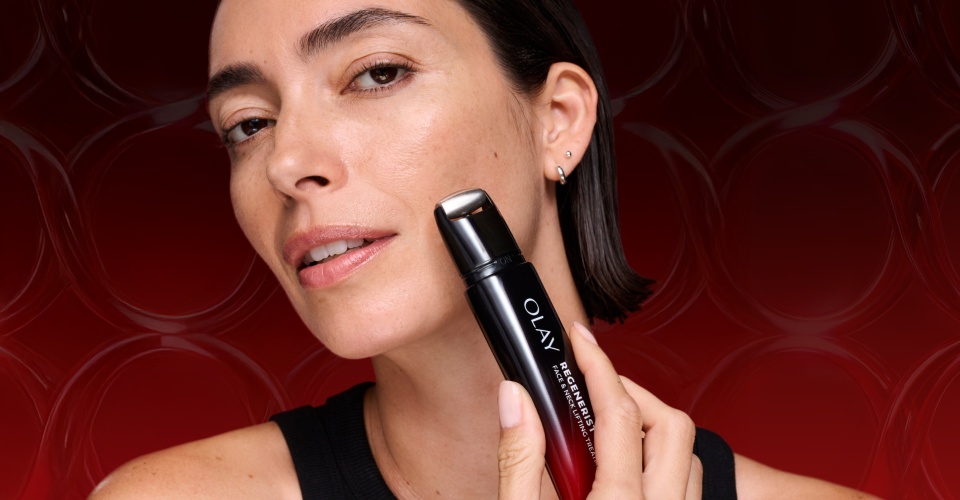  Caucasian woman holding up the tip of the Olay Face and Neck Treatments roller against her left cheek