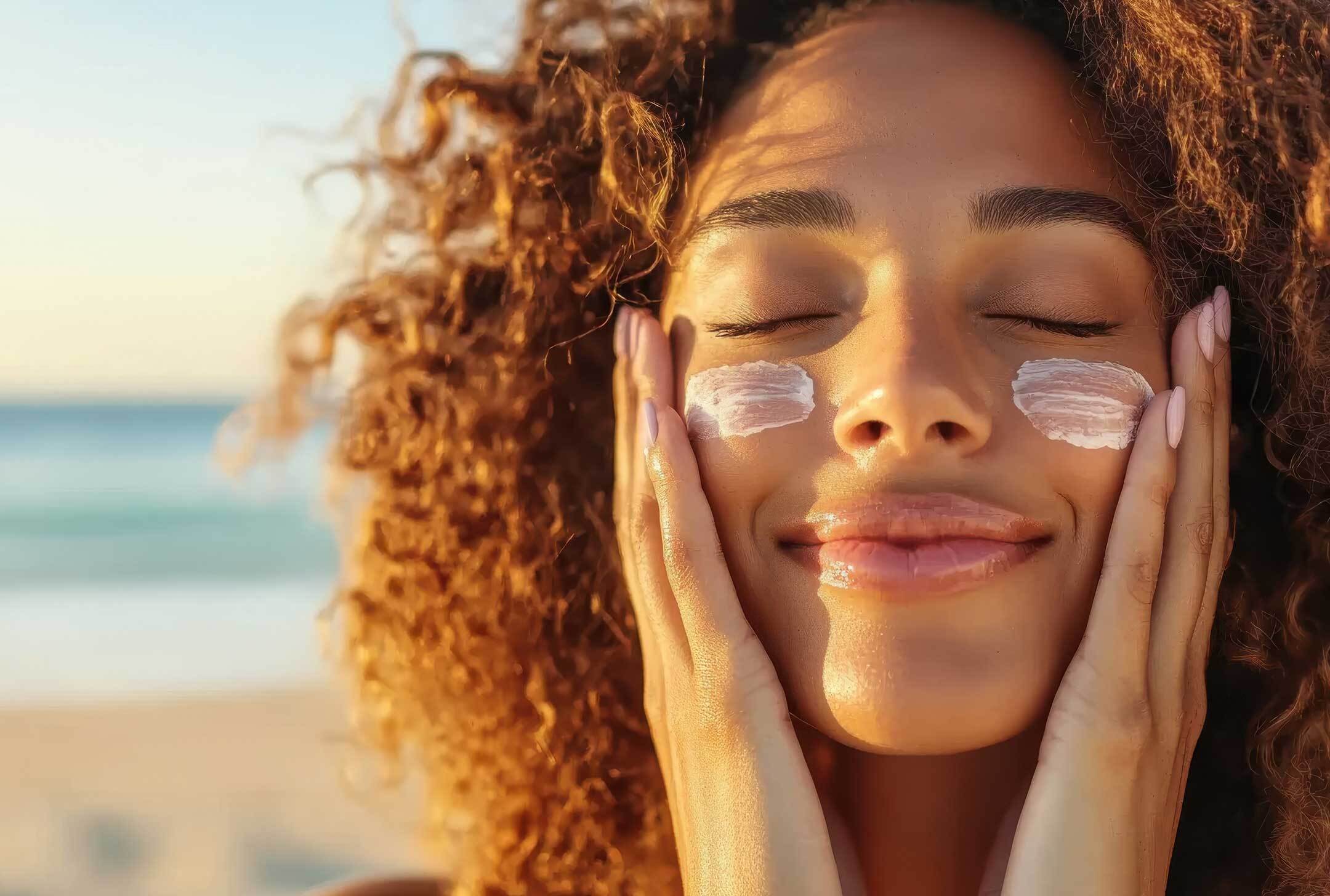 Woman on a beach with her hands clasped on her cheeks and a swipe of sunscreen under her eyes.