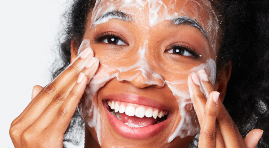 African American woman rubbing cleansing foam over her face and smiling.