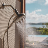 Side view of the Nebia Corre Four-Function Handshower Brushed Nickel spraying water close to a window