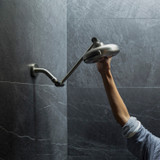 Nebia Adjustable Shower Arm Chrome with a chrome showerhead installed and a hand moving it in a dark gray background