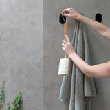 Nebia Multi-Purpose Hook Set Matte Black three pieces in use holding a towel and a loofah with a pair of arms reaching for the loofah in front of a  gray background