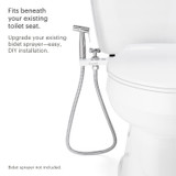 Image of a bidet attachment designed to fit beneath an existing toilet seat, shown installed with a flexible hose and nozzle for a hand-held bidet sprayer. The image includes text that reads: 'Fits beneath your existing toilet seat.