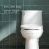 “Swash CL150 non-electric bidet toilet seat installed on a white toilet, shown closed with a wrap-over lid design that fully covers the seat, creating a sleek, streamlined look against a green tiled wall.