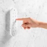 Brondell Coit remote control mounted on granite wall with hand pressing button.