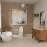 Modern bathroom with warm beige tiled accent wall, featuring the Coit Integrated Smart Bidet Toilet centered beneath a large abstract painting, alongside a freestanding bathtub, wooden double vanity with gold fixtures, and terrazzo flooring.