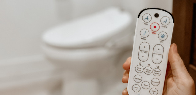 Close-up view of luxury bidet remote control with installed bidet in background