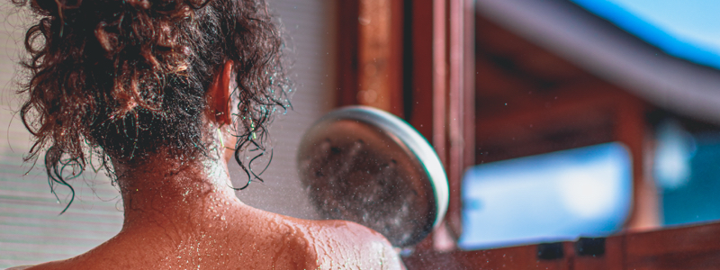 Woman in shower holding the Brondell water-saving shower heads made with recycled plastics.