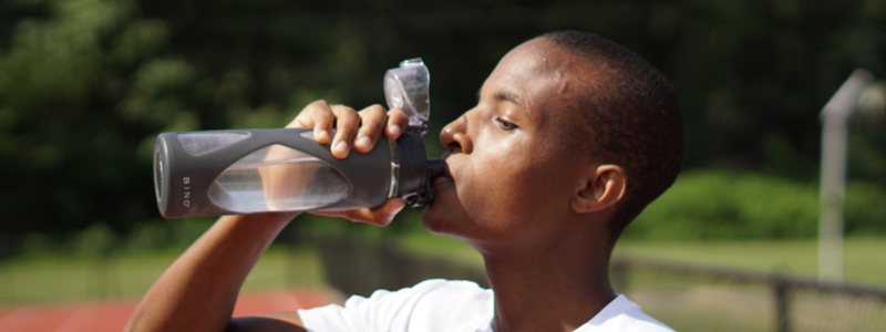 male teen athlete drinking from water bottle on an outdoor track field