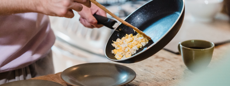 closeup view of male hands cooking scrambled eggs in a frypan and plating for two