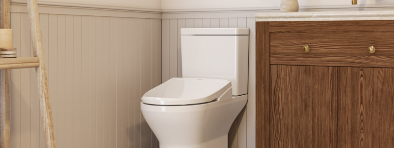 A sleek white Wash Thinline T44 Luxury Bidet Toilet Seat with Remote Control is installed in a modern bathroom, next to a wooden cabinet with brass handles, highlighting minimalist design.