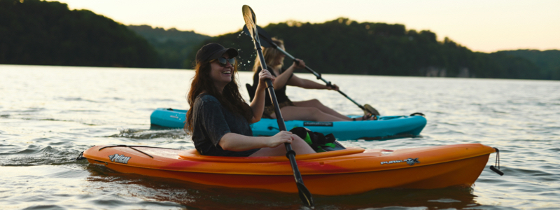 Two women in kayaks with a mountain backdrop.