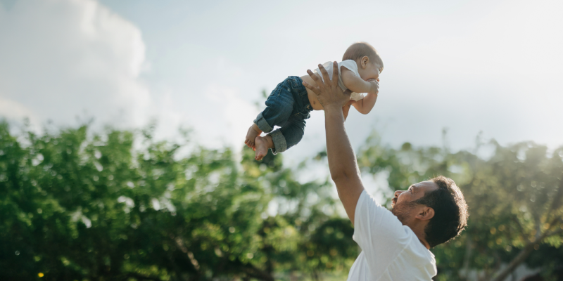 Dad holding baby above his head in a park setting