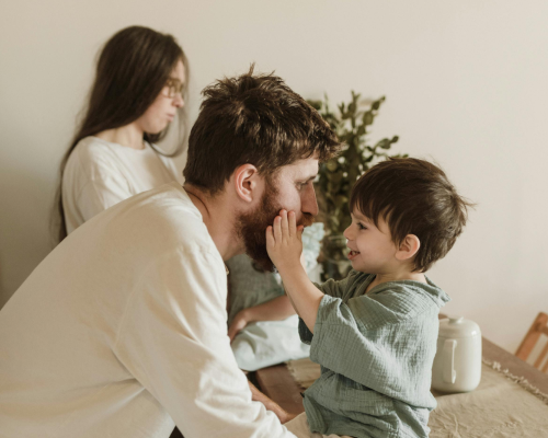Child sitting on table holding Dad's face with daughter in background